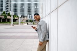 Man using smartphone leaning against wall