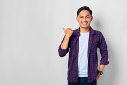 Asian male in grey studio with thumb to the side