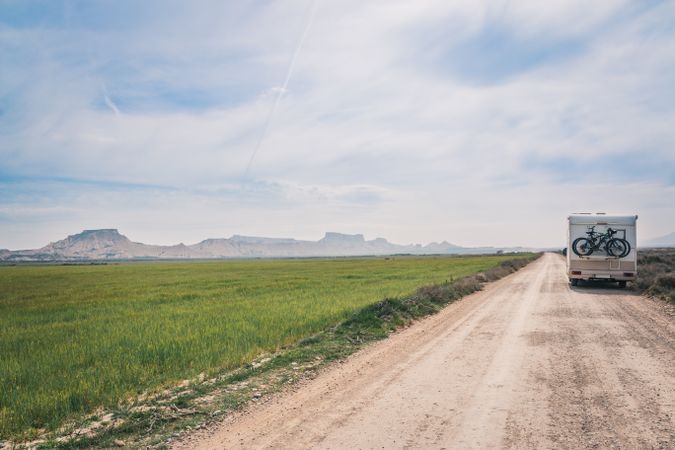 trailer on empty road between fields with vegetation