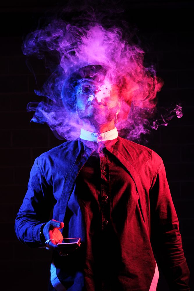 Black man exhaling smoke on dark background