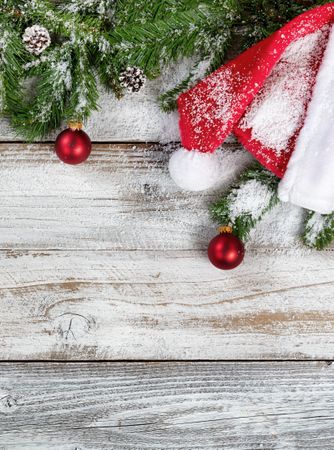 Snowy Christmas fir branches with traditional Santa hat and ornaments on rustic wooden background