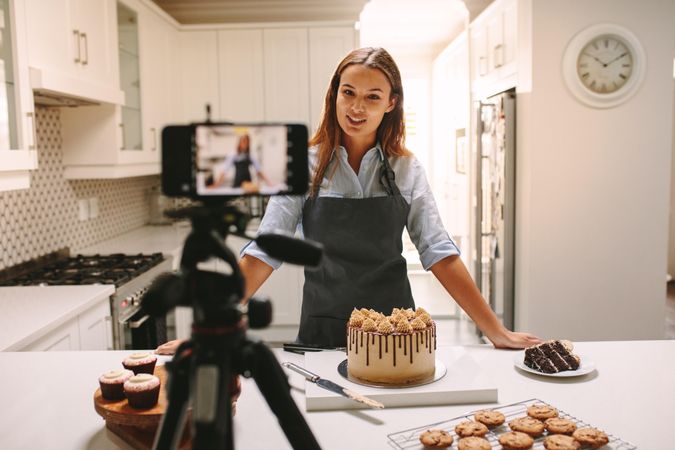 Female pastry chef vlogging with mobile phone mounted on tripod in kitchen