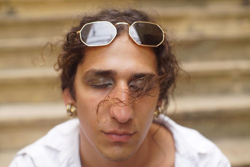 Portrait of man wearing earrings and eye shadow and closing his eyes