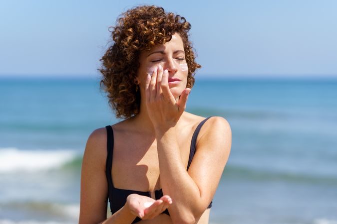 Young female smearing cream on face protecting from sunburn