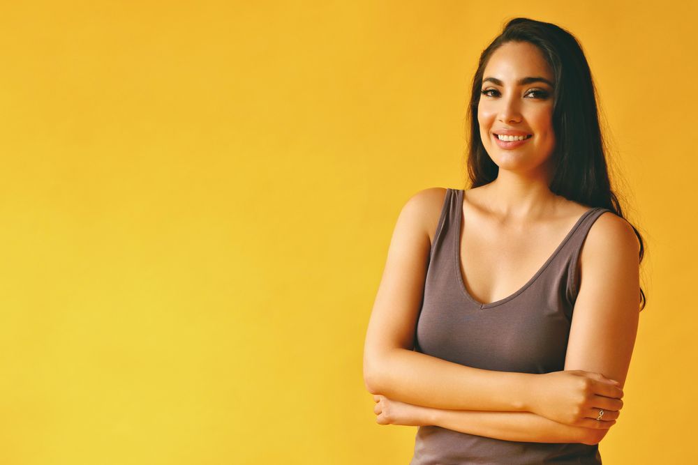Smiling Hispanic woman standing and looking at camera in yellow room, copy space