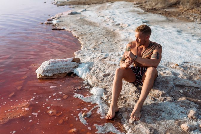 Tranquil man in swimwear sunbathing on shore of pink lake