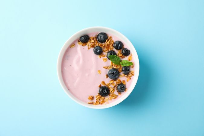 Yogurt with granola, blueberry and mint on color background