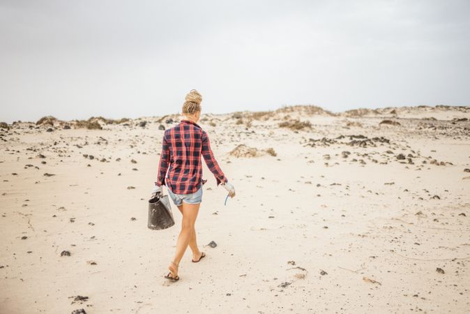 Content modern woman picking litter from sandy seashore