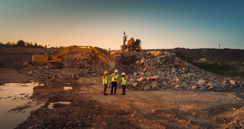 Aerial Drone Shot Of Construction Site With Excavators On Sunny Day: Diverse Team of Real Estate Developers Discussing Project. Engineer, Architect, Inspector Talking About New Building, Using Tablet.
