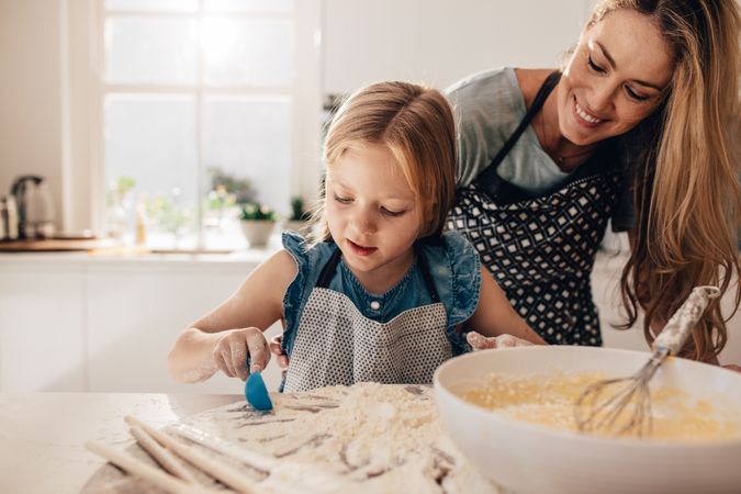 Young girl scooping baking ingredients into bowl with mom