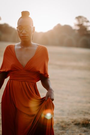 Woman in orange v neck dress standing in grass field