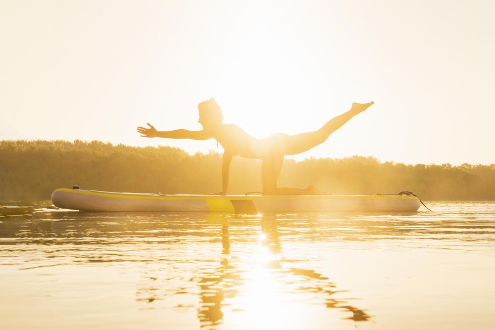 Woman doing yoga balance on paddle board at dawn