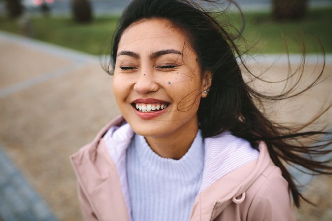 Young woman in warm coat smiling with eyes closed