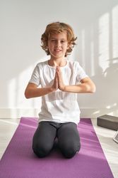 Cute boy sitting on yoga mat with hands in Namaste