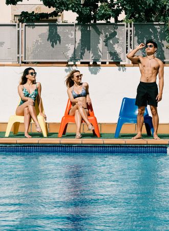 two young women looking at a handsome man by the pool