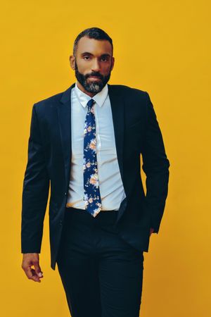 Serious Black male in suit with floral tie in yellow studio