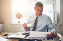 Man in business attire sipping coffee while looking over documents 4NPoD0