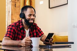 Black man using smartphone while having coffee at home