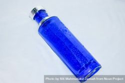 Blue perfume bottle with water droplets on light background with copy space bE9pvV