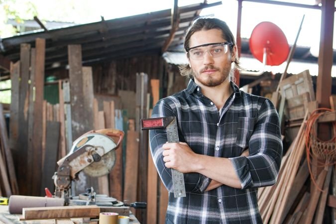 Man in safety glasses holding ruler in woodshop