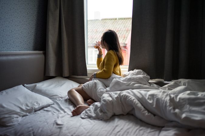 Anonymous female on vacation delighting in view in window while drinking tea in morning