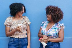 Two Women drinking coffee in the street, talking and laughing.