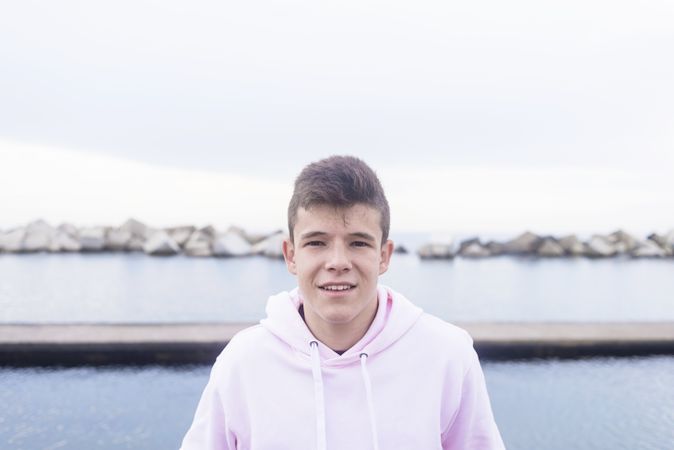 Young male teenager standing on rock breakwater while looking at camera