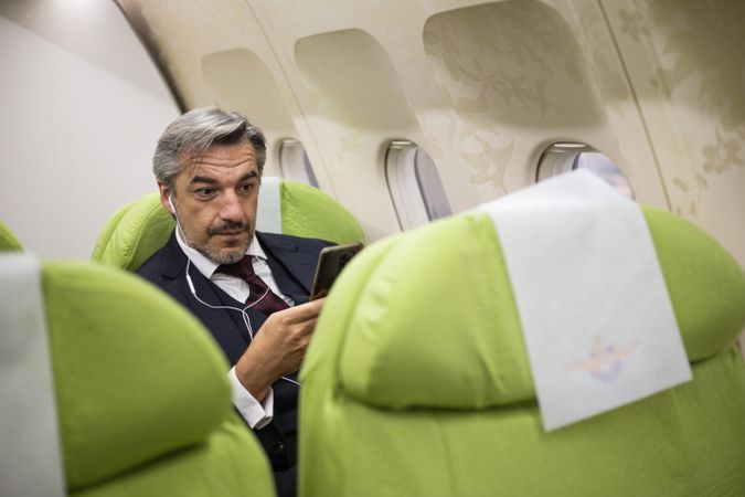 Male using smart phone with ear buds in flight