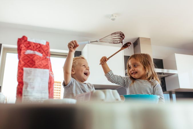Cute little boy and girl holding whisk and spatula having fun while cooking in the kitchen