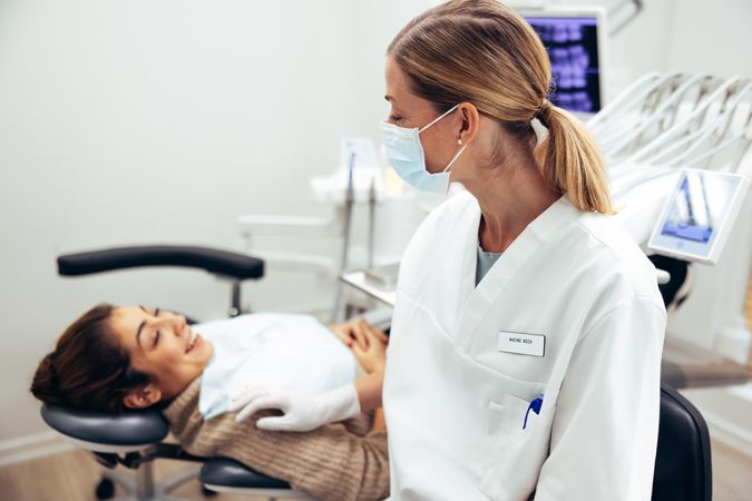 Female dentist wearing face mask talking with patient in dentist's chair