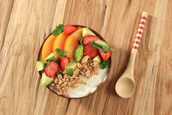 Granola with Greek yogurt, fresh fruit and mint garnish on wooden table
