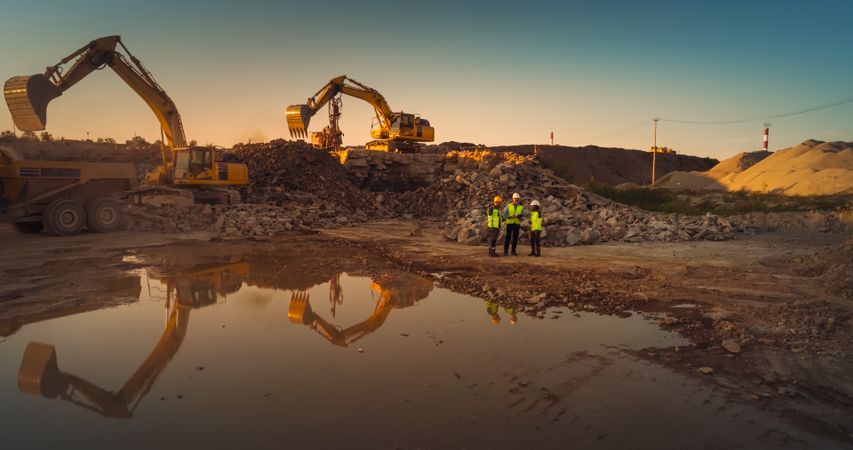 Aerial Drone Shot Of Construction Site With Heavy Machinery On Sunny Day: Diverse Team of Real Estate Developers Discussing Project. Civil Engineer, Architect, Urban Planner Talking, Using Tablet.
