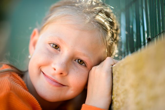 Gentle girl leaning on fence in sunshine