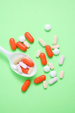 Top view of various pills with plastic spoon on green table