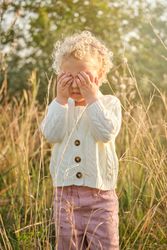 Adorable girl covering eyes with hands in sunny garden