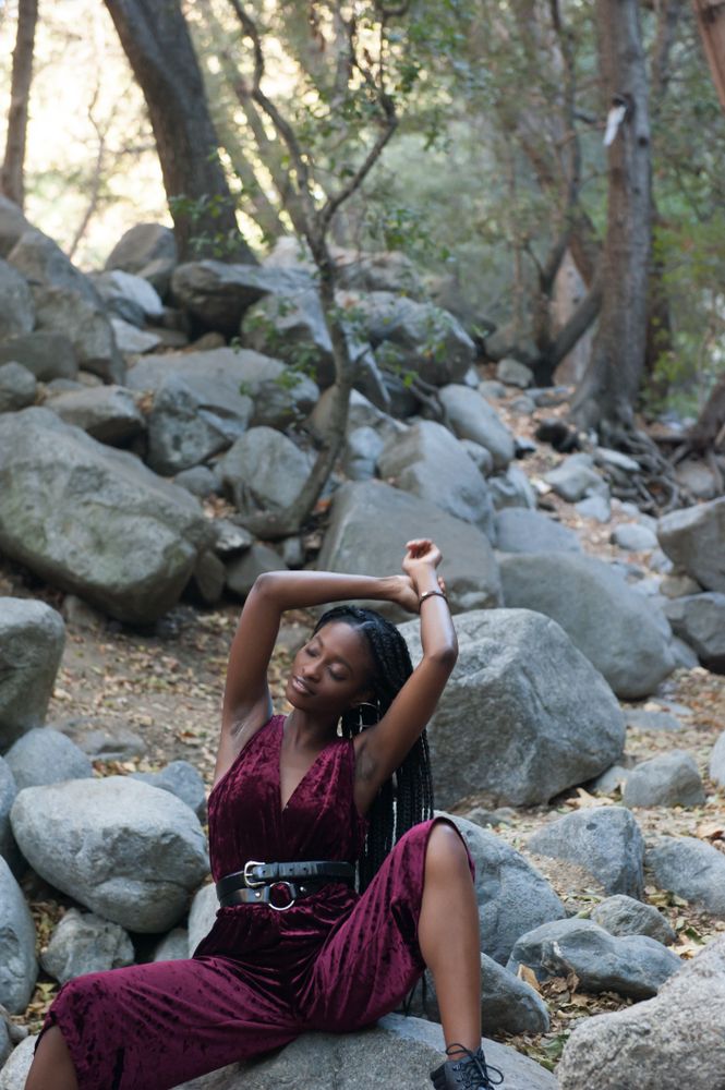 Fashionable woman with braids sitting on rocks outside in the woods with her arms above her head