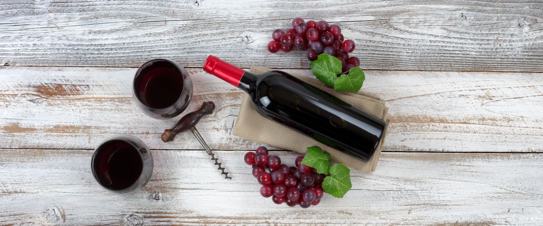 Red wine ready to drink with full bottle and grapes on weathered wooden boards