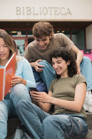 Happy young diverse friends sharing smartphone in campus