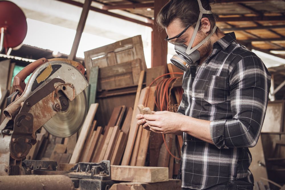 Male carpenter wearing protective mask using electric circular saw cutting wood