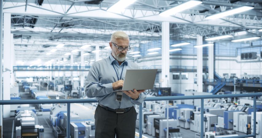 Thoughtful Mature Engineer Monitoring and Analyzing Conditions at a Pristine Modern Electronics Factory with Automated Mobility Robots Working with the Help of Artificial Intelligence Software