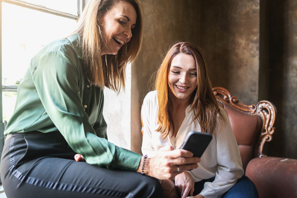 Two women smiling at something on a smartphone screen
