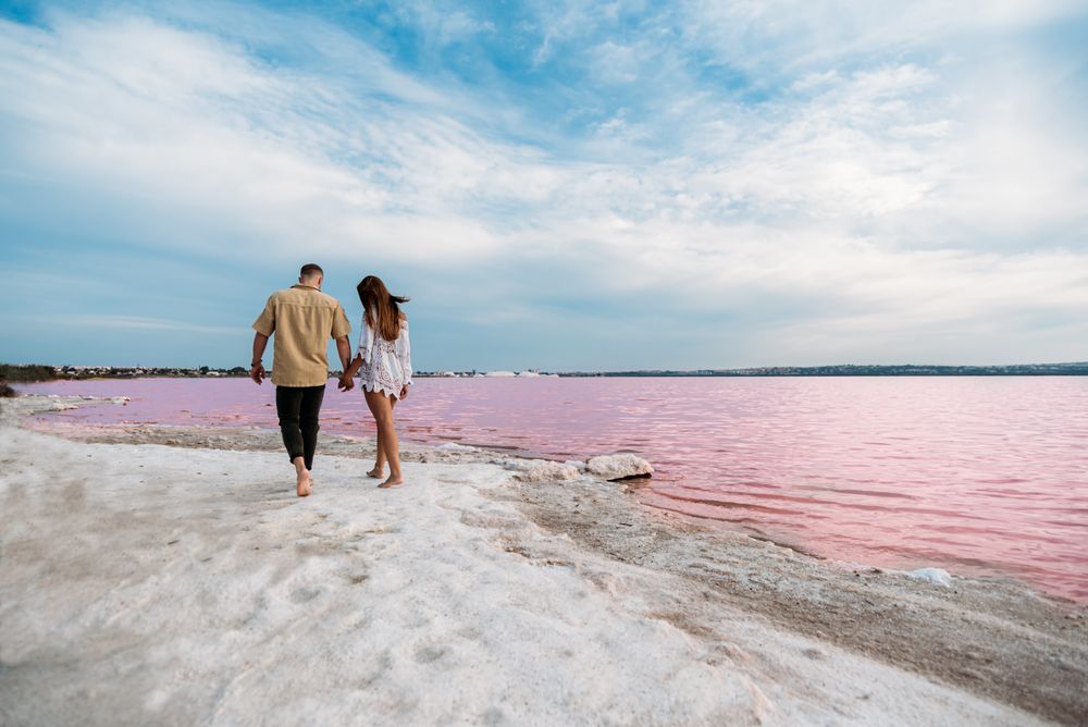 back view of adorable couple walking on an amazing beach with pink water