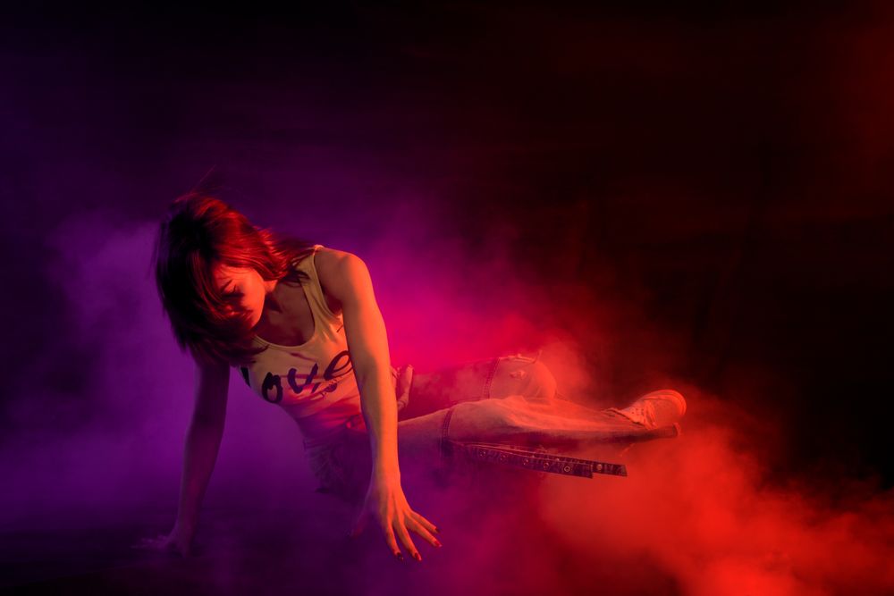 Young woman break dancing in colorful smoke