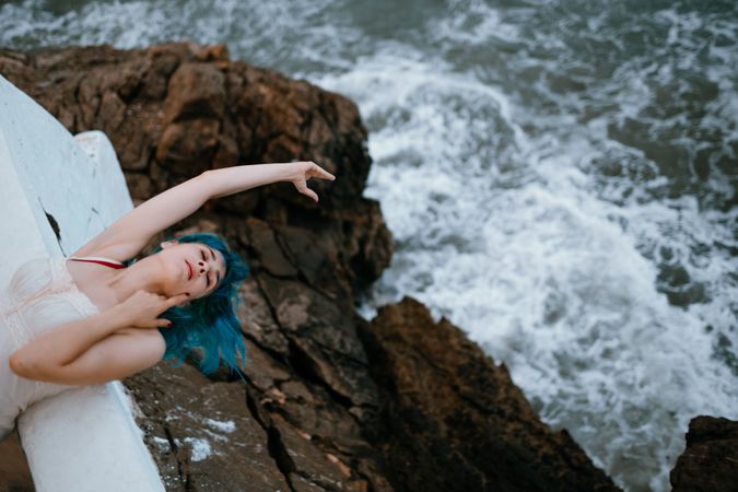 Gracious woman in sundress lying on back on parapet and reaching out for ocean