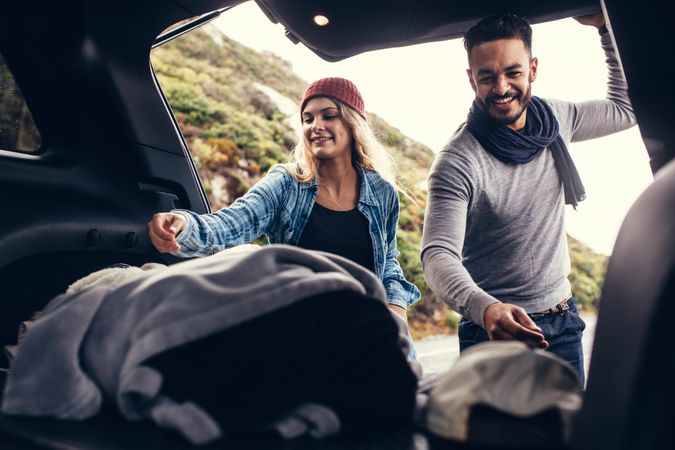 Beautiful couple packing luggage into back of car