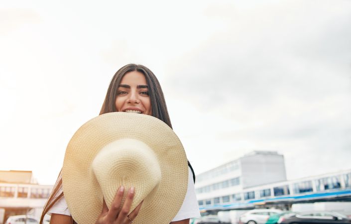 Smiling woman hiding her lower face with straw hat outside