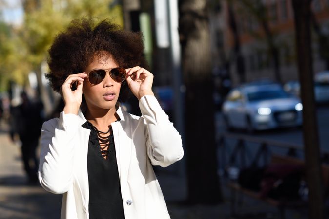 Serious stylish female putting on aviators sunglasses on street