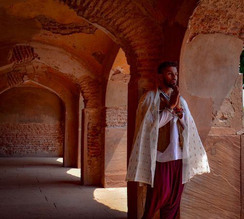 Man in light traditional Indian outfit standing beside pillars