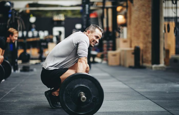 Man smiling on gym floor with barbell