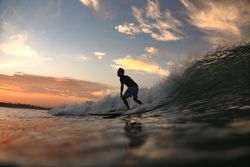 Man on surf board on waving water at sunset